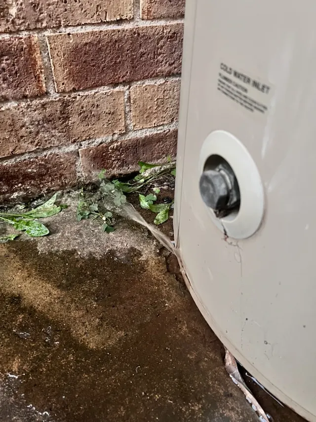 Electric storage hot water tank leaking from the base against a brick wall